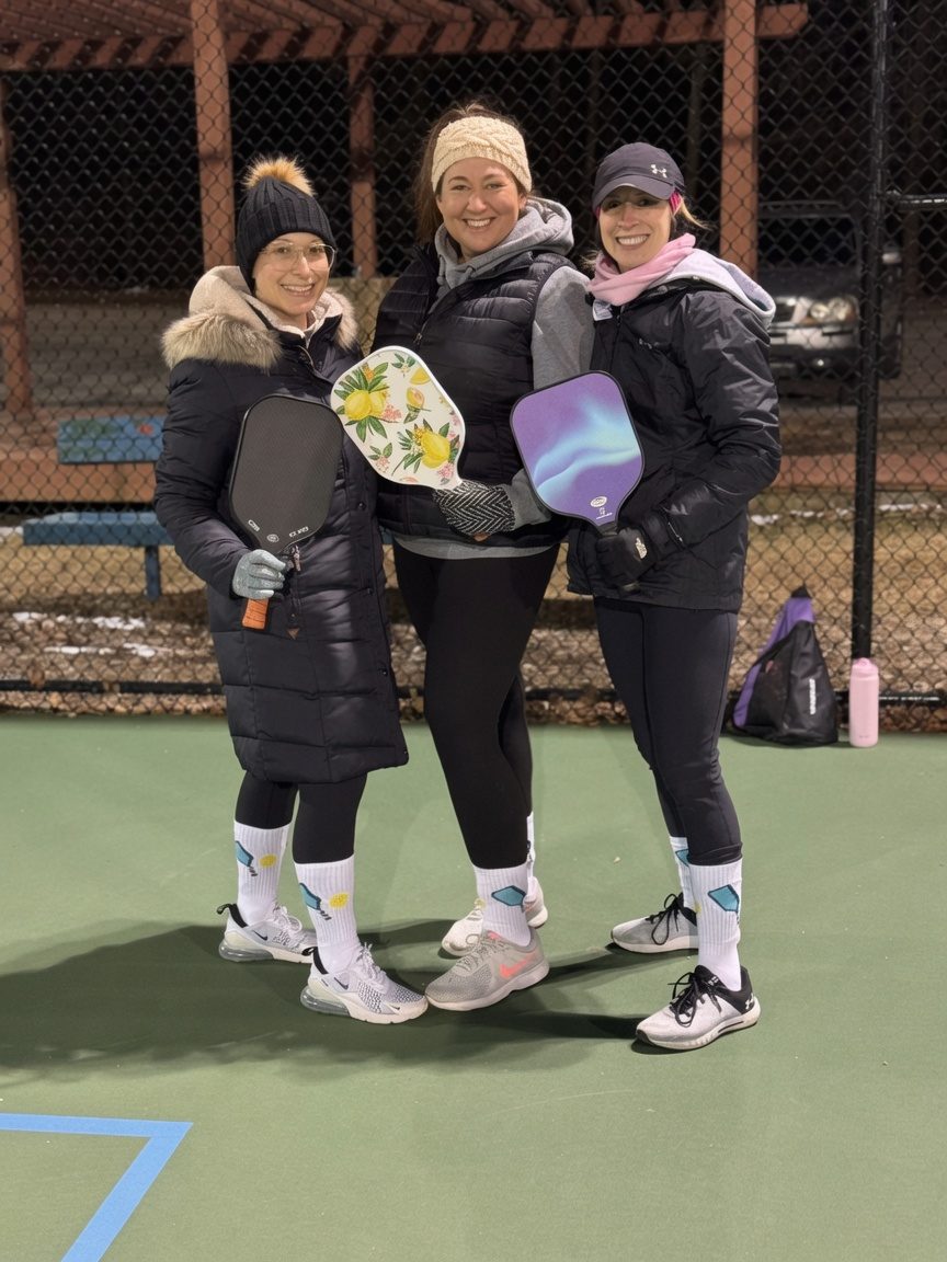 Three pickleball players smiling with their paddles at the Neills Creek courts behind Harnett Central after a clinic